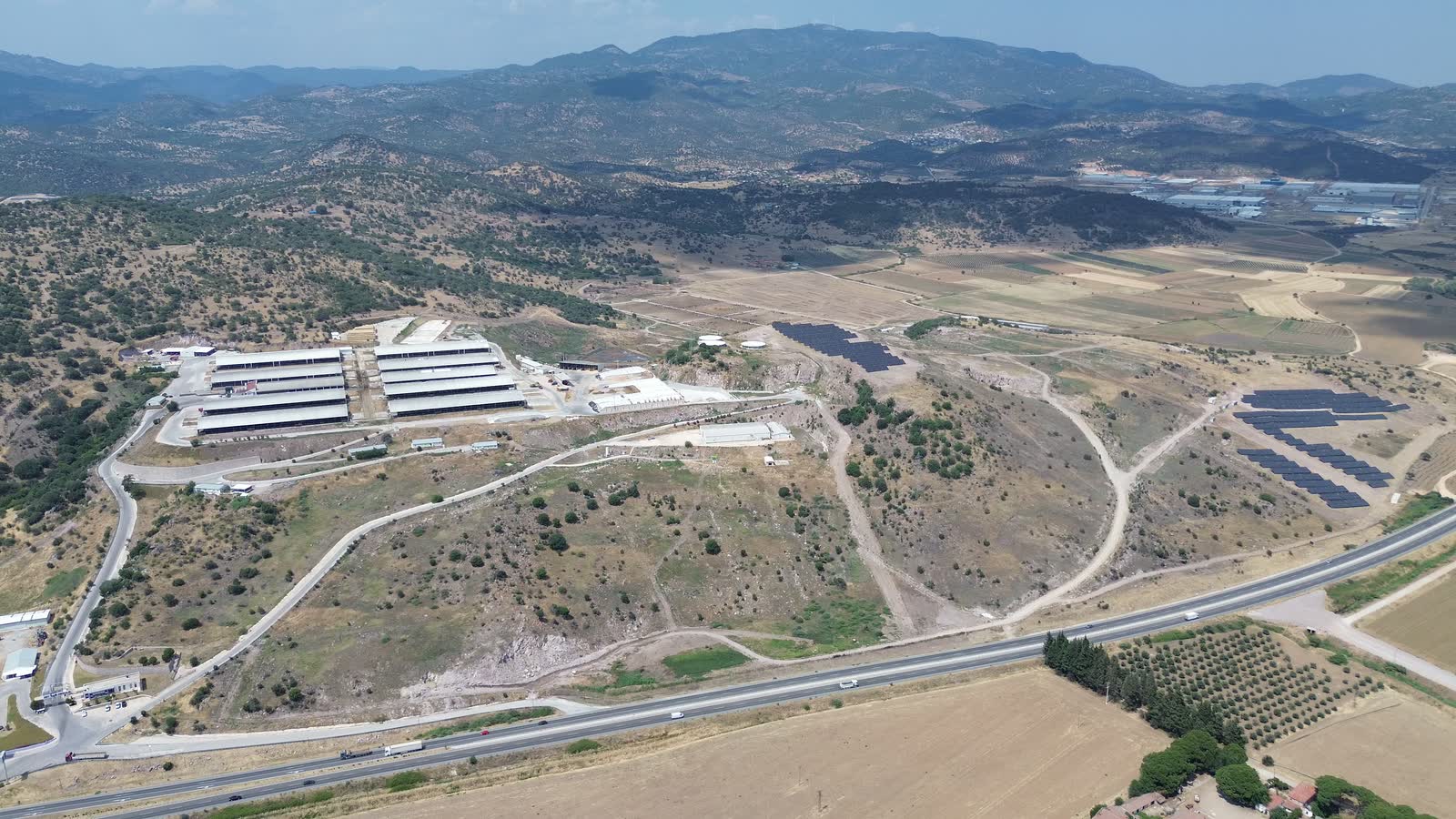 Süt Kardeşler tesisinin havadan panoramik görünümü: barınaklar, güneş enerji santrali ve arkada dağ silsilesi